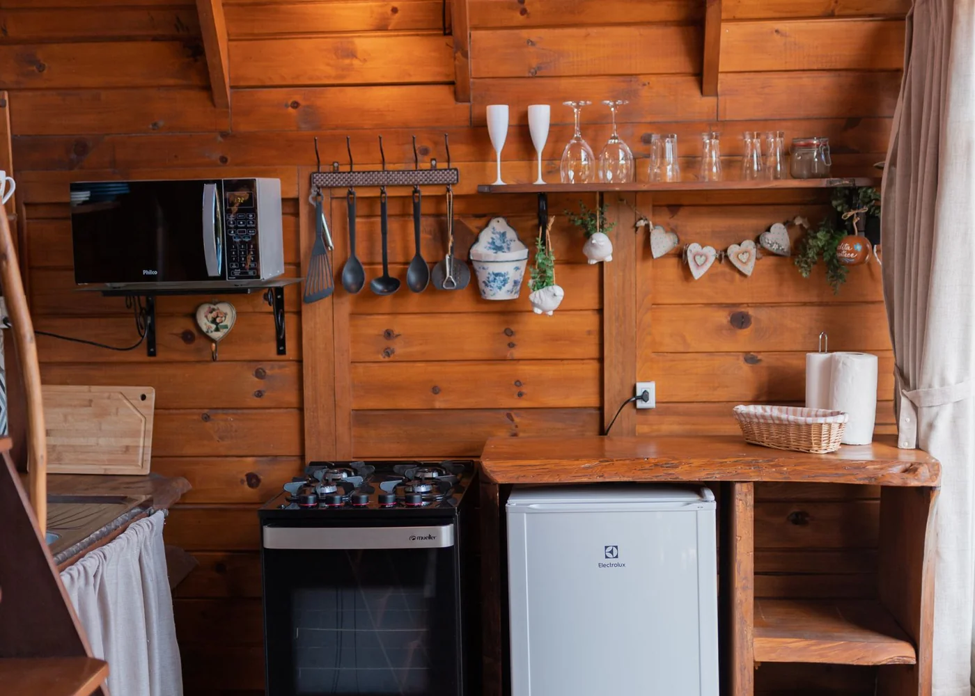 A compact wooden kitchen with a cooker, fridge and hanging utensils.