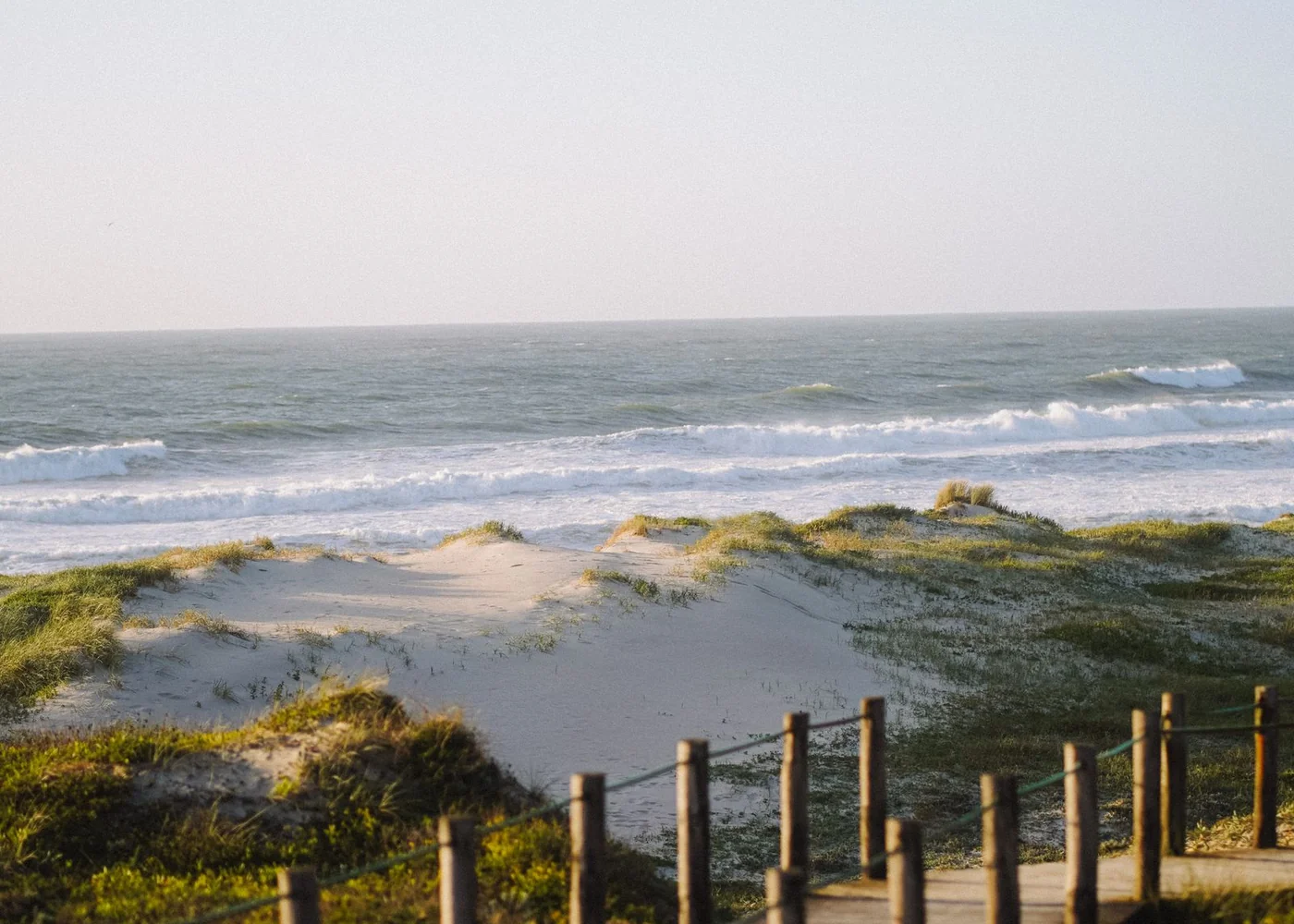 A wooden access route through low dunes towards the sea.