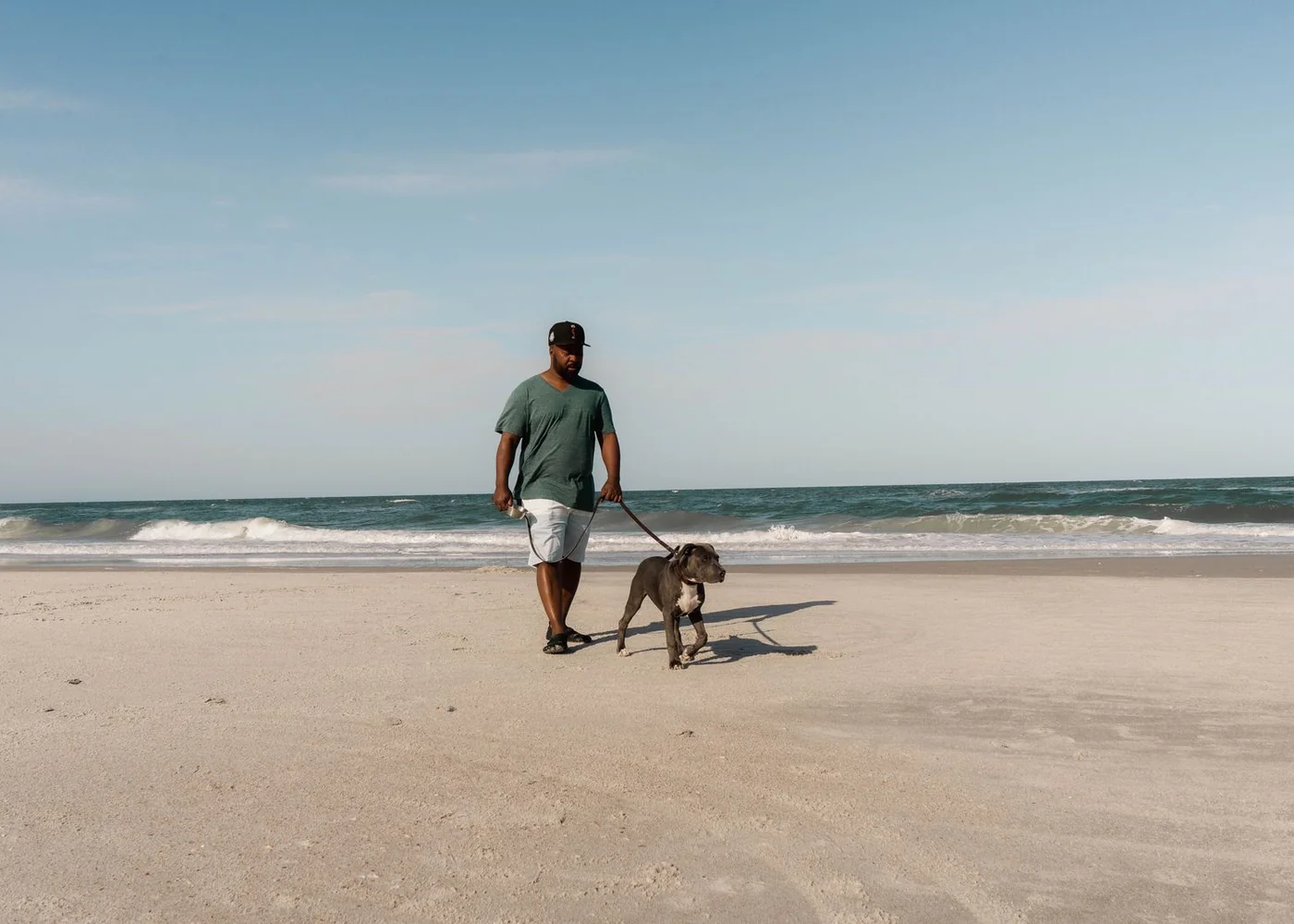 A person walking a dog on a lead along the sand.