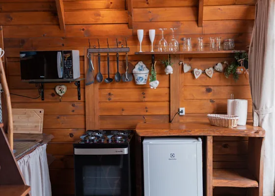 A compact wooden kitchen with a cooker, fridge and hanging utensils.